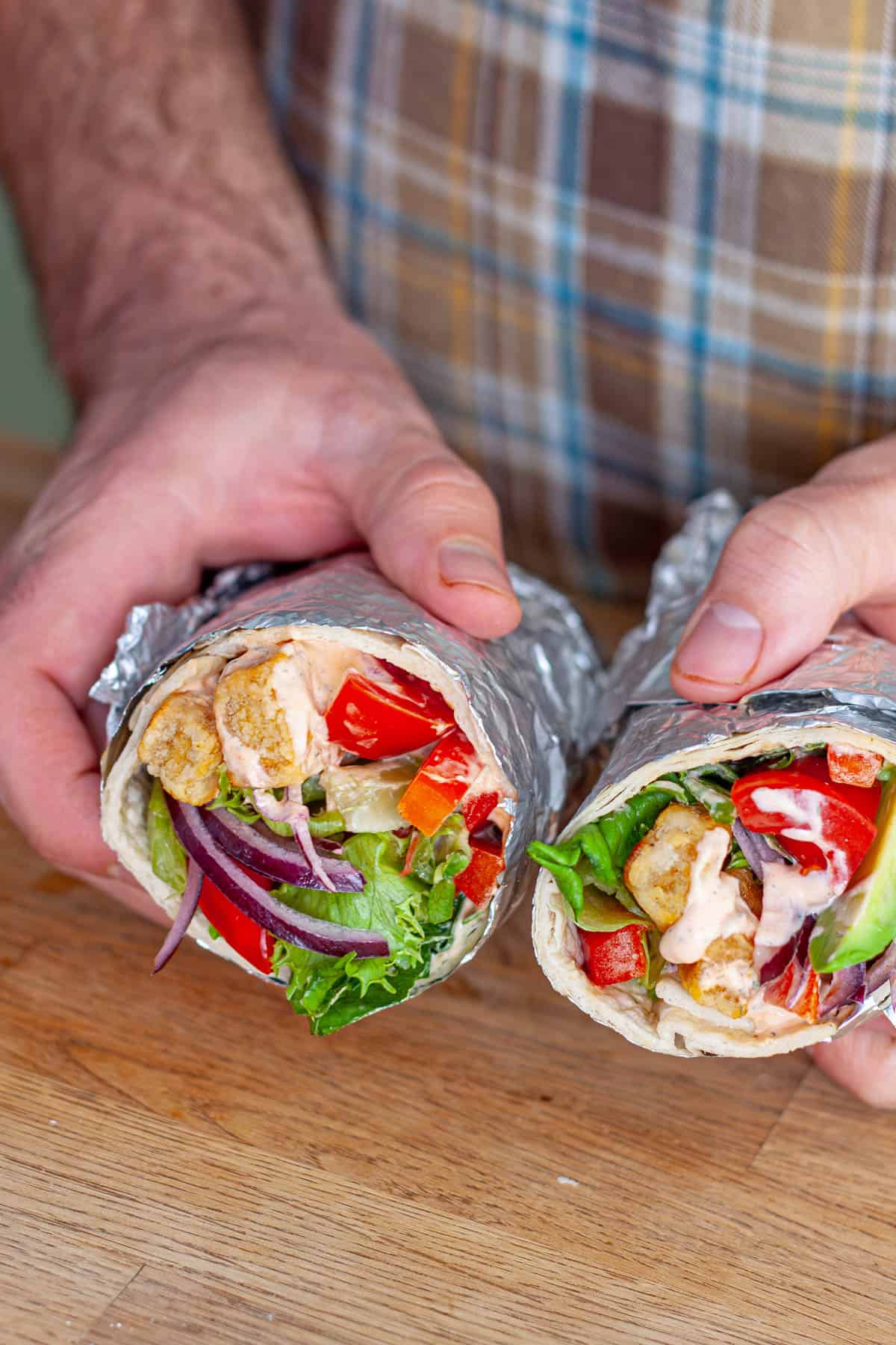 Hands holding crispy buffo tofu wraps cut in half.