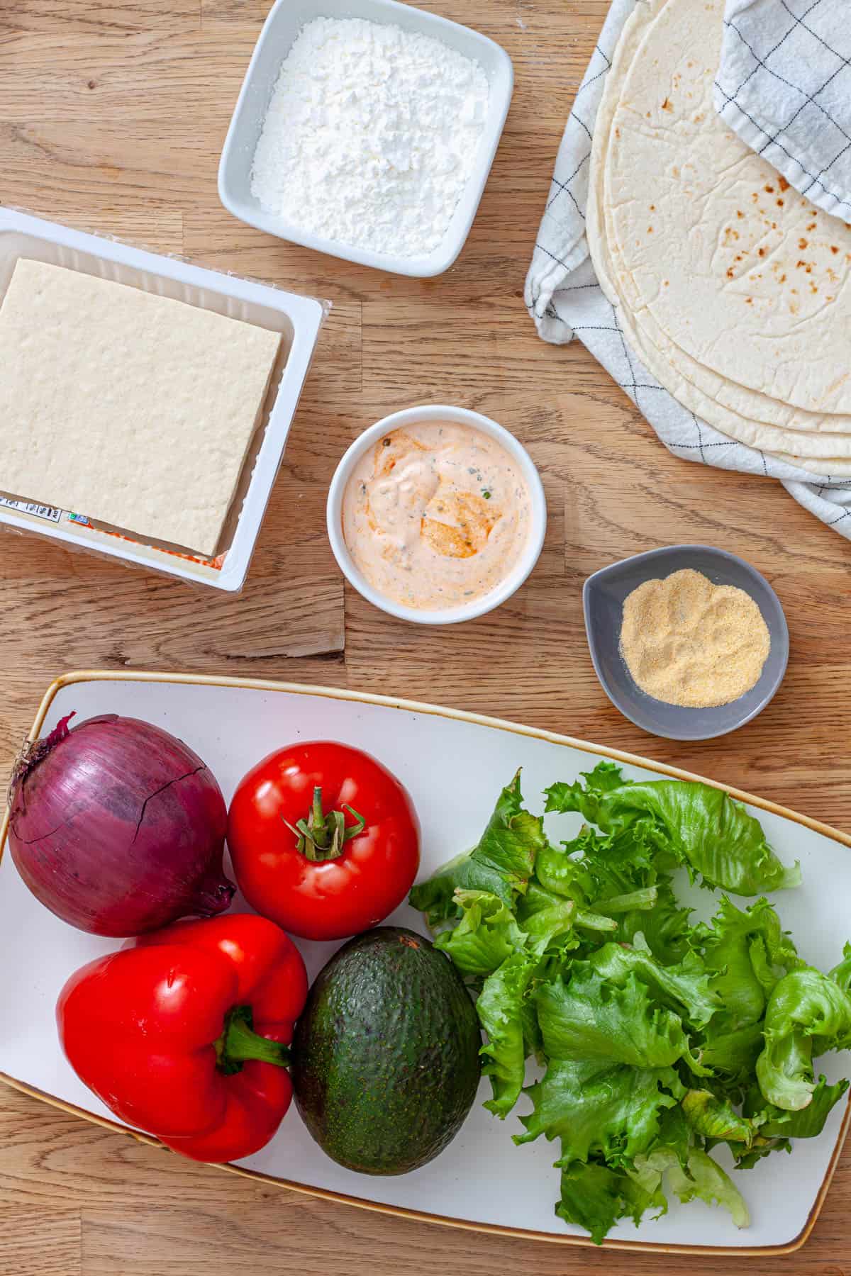 Ingredients for crispy buffalo tofu wraps on a butcherblock cutting board.