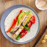 A plate with crispy buffalo tofu wrap topped with avocado, red peppers, lettuce, red onions and a homemade buffalo ranch sauce.