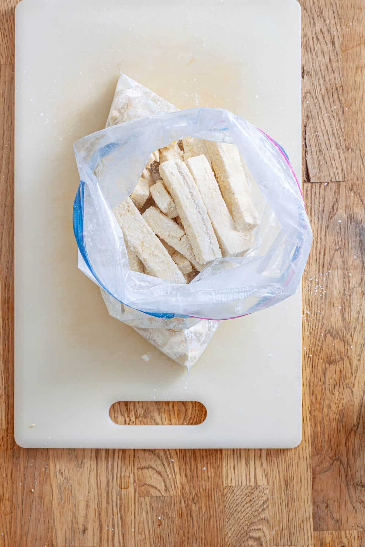 Strips of tofu in a zip-top bag with cornstarch and seasoning getting ready to be baked.