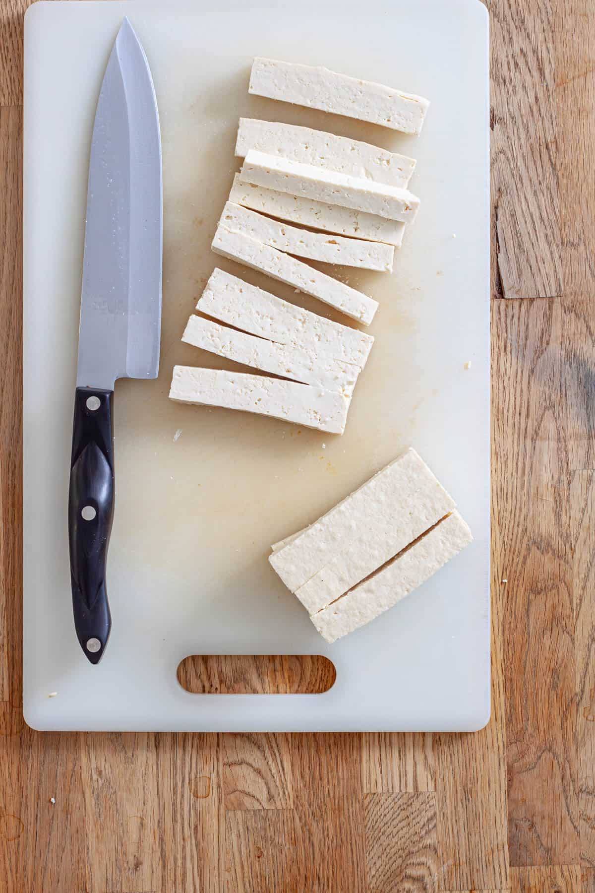 Tofu on a cutting board getting cut into strips for tofu wraps.