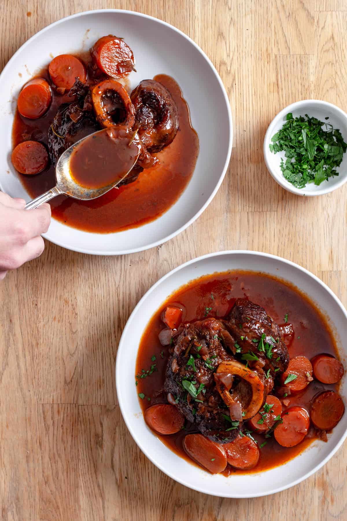 A couple servings of braised beef shanks on serving bowls with a spoon pouring on some braising liquid.