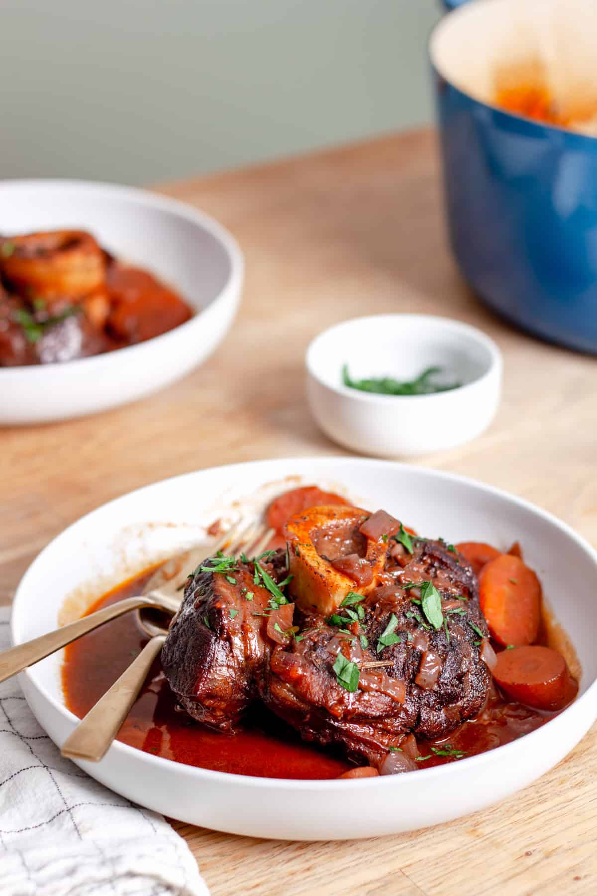 A serving of braised beef shank on a serving bowl with carrots and braising liquid garnished with parsley.