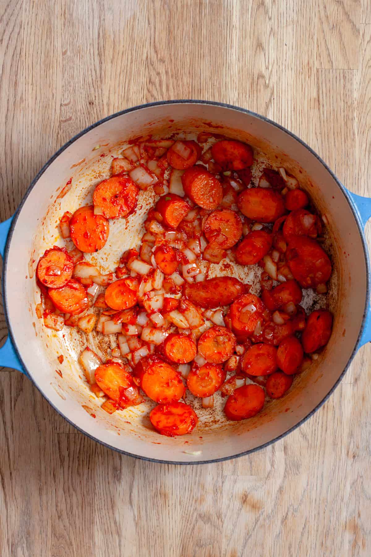 Onions and carrots cooking in a dutch oven with tomato paste and garlic.