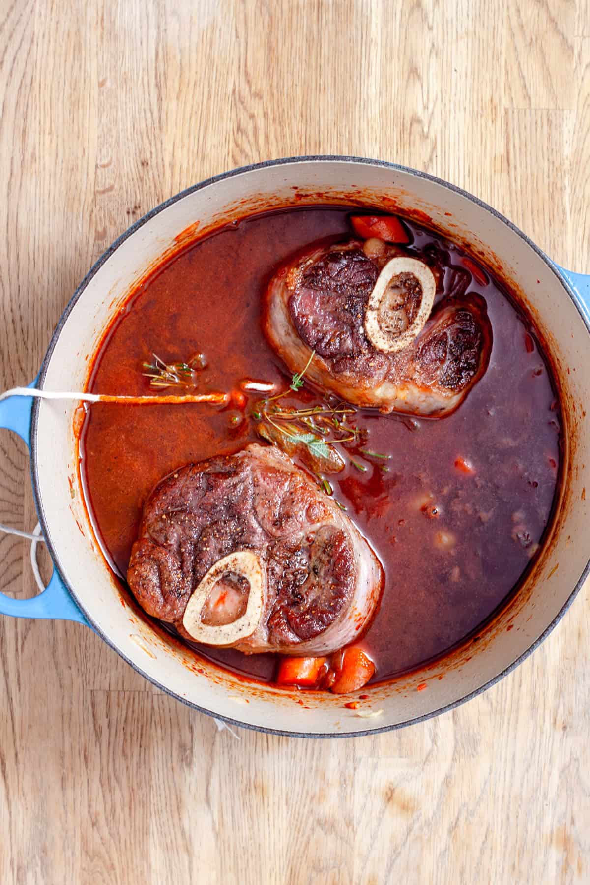 Seared beef shanks in braising liquid in a Dutch oven.