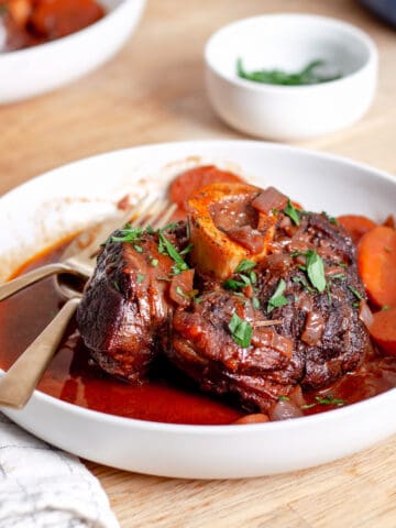 A serving bowl of braised beef shanks topped with chopped parsley.