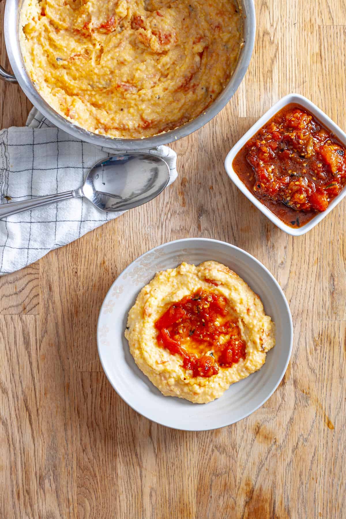 A small bowl with a serving of cheesy polenta topped with roasted smashed tomatoes.