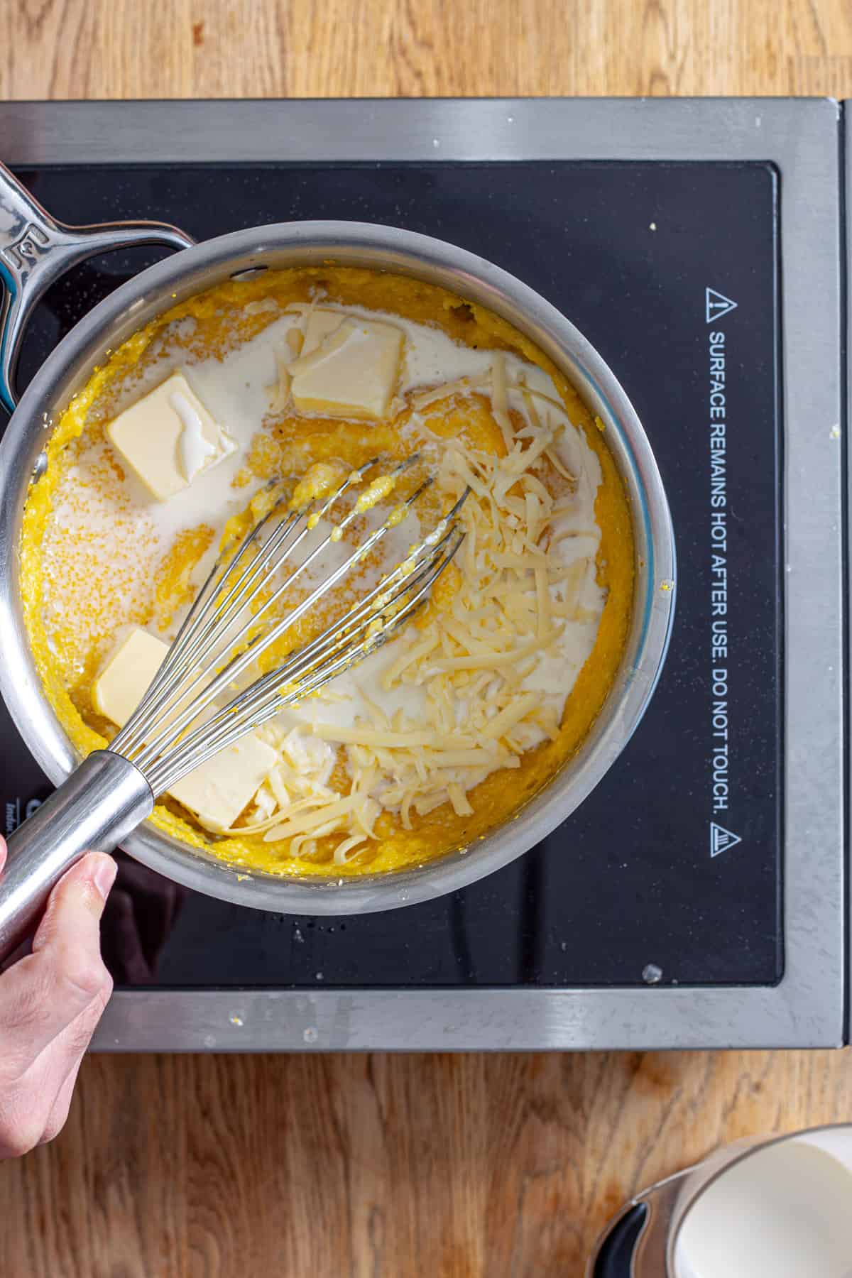 Butter, cheese and cream getting whisked into polenta in a medium saucepan.