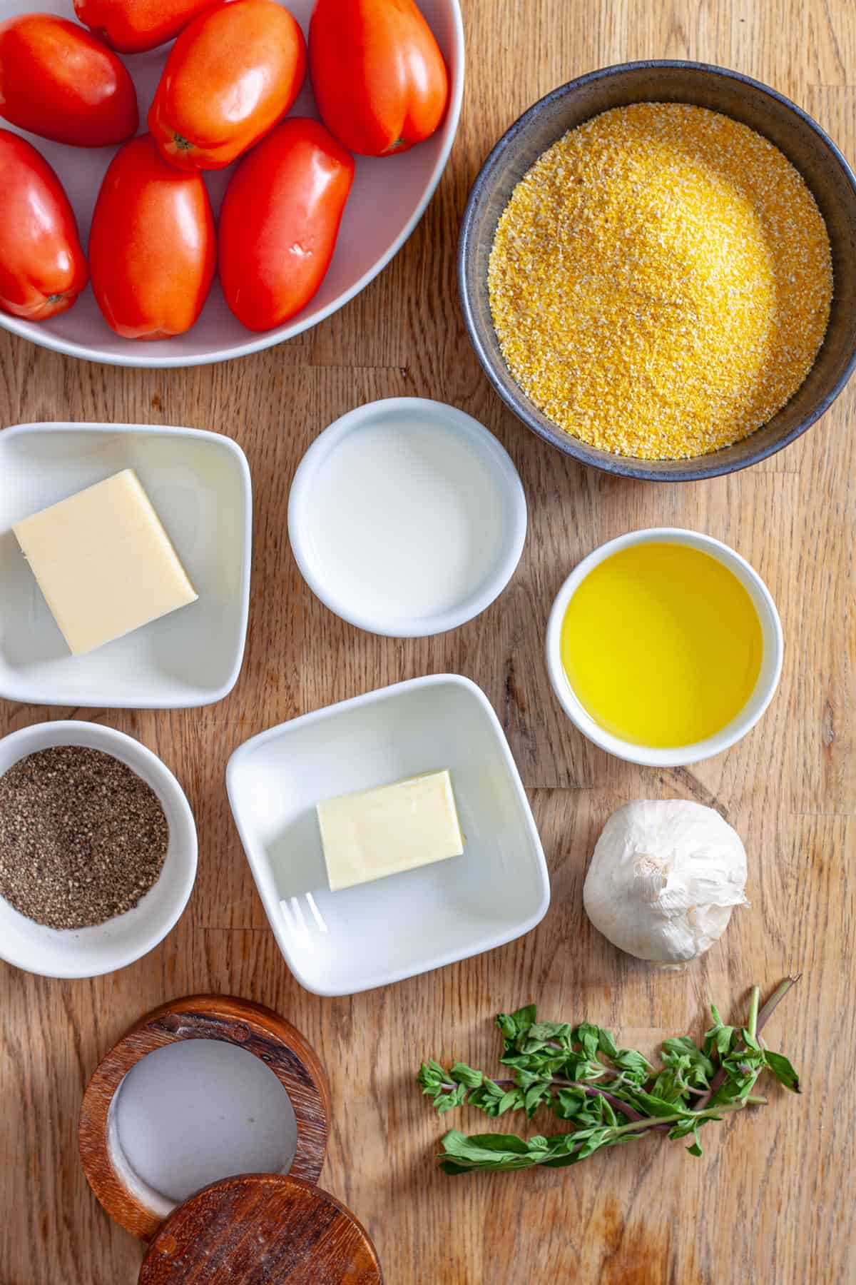 Ingredients for cheesy polenta with roasted tomatoes on a butcherblock table.