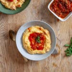 A couple bowls with cheesy polenta topped with smashed roasted tomatoes and oregano.