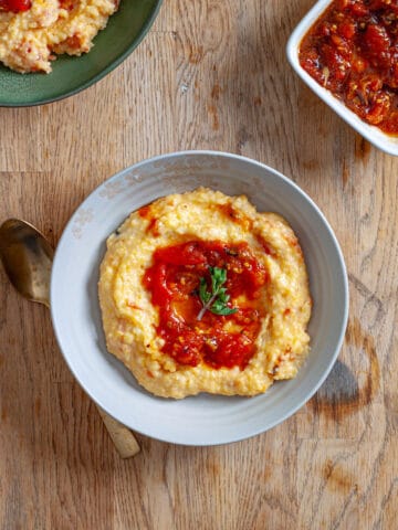 A couple bowls with cheesy polenta topped with smashed roasted tomatoes and oregano.