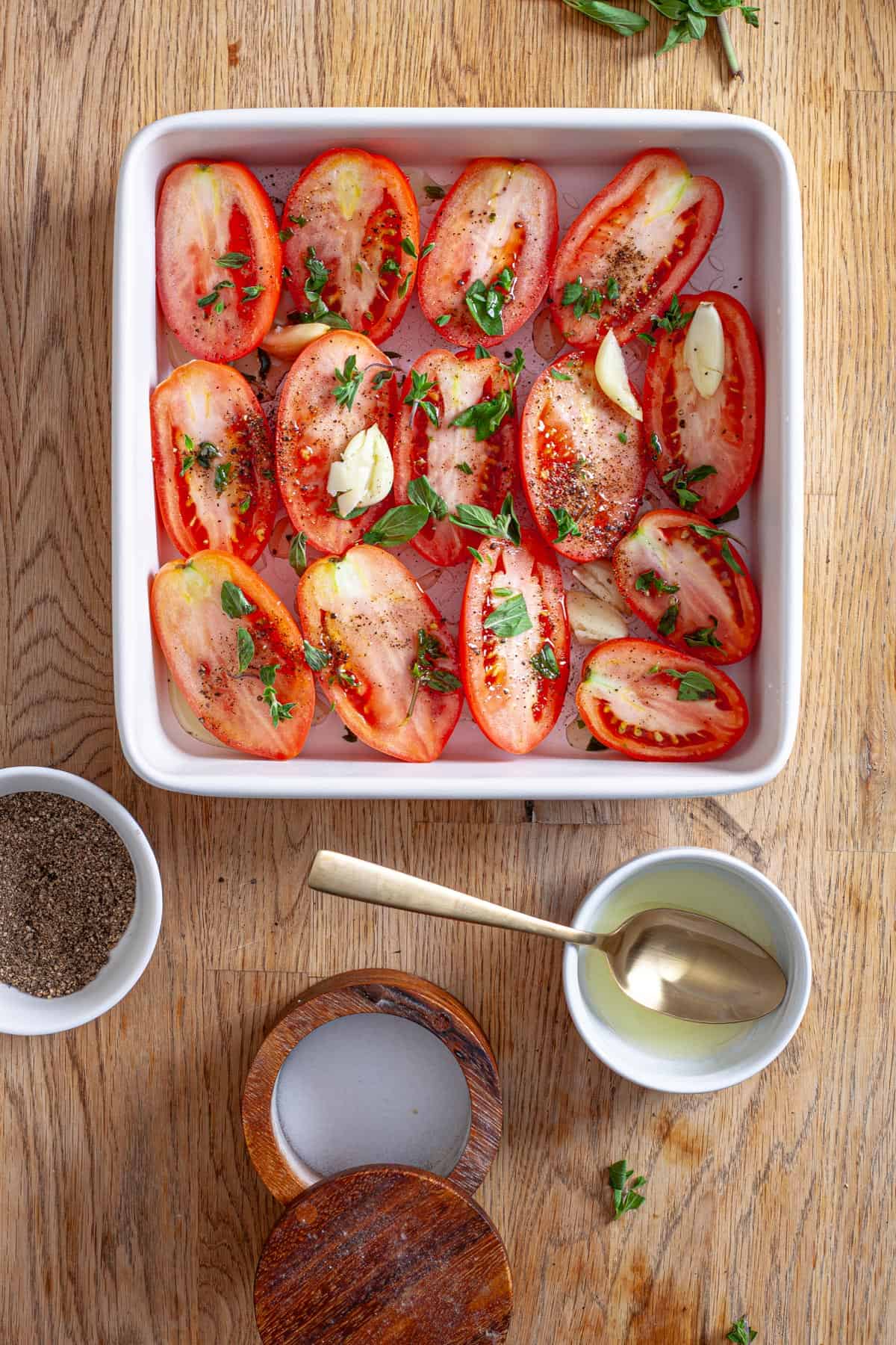 Tomatoes cut in half topped with oregano, oil and garlic in a baking dish.