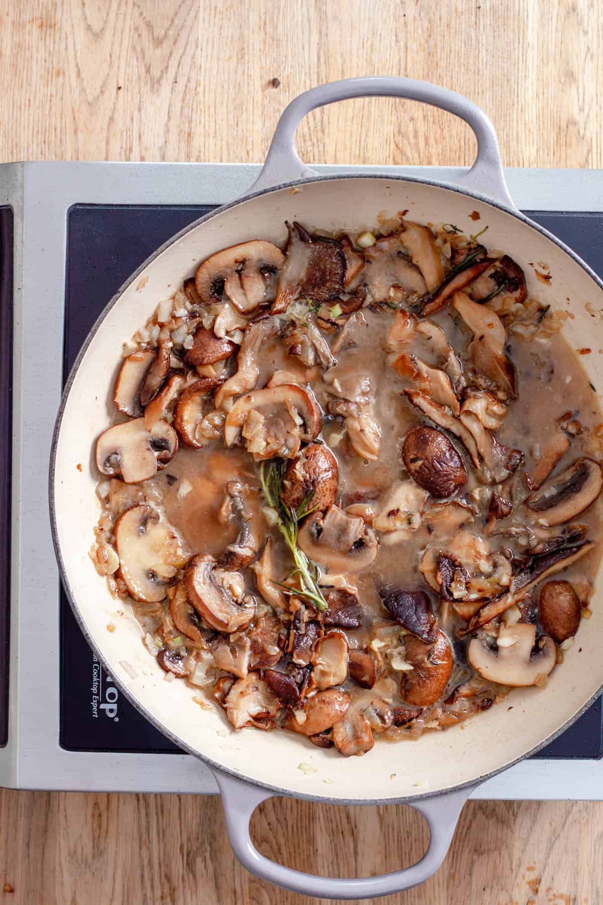 Mushrooms cooking in a large skillet with onions, garlic, herbs and white wine.