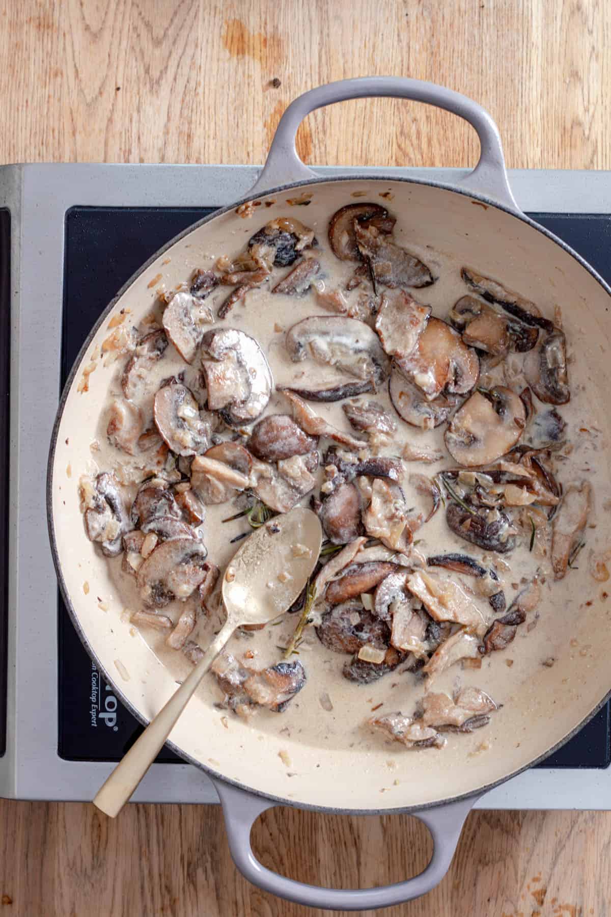 A mushroom sauce cooking in a large skillet with white wine, cream and herbs.