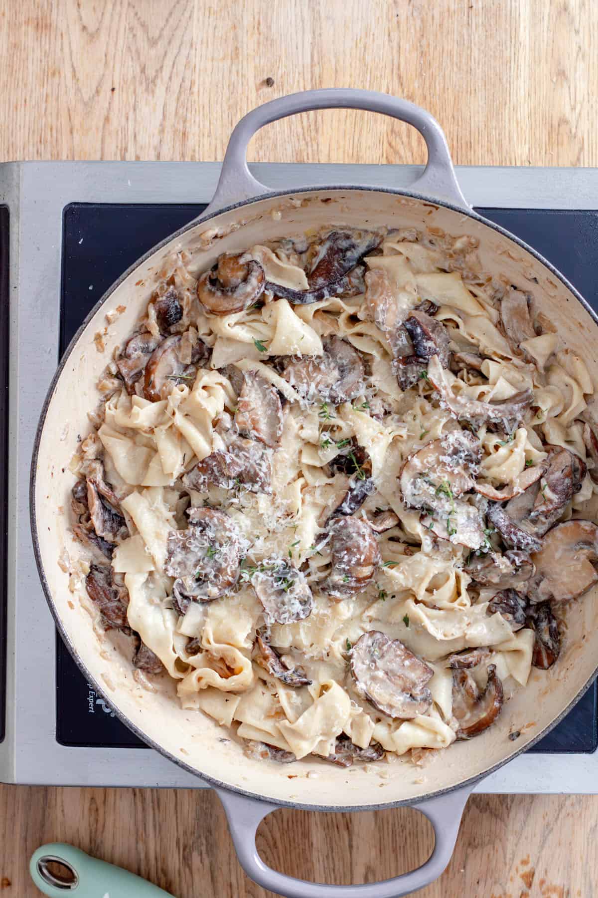 Mushroom pappardelle cooking in a large skillet garnished with parmesan cheese.