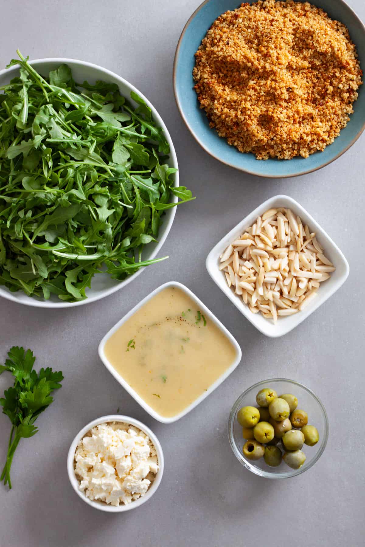 Ingredients for quinoa and arugula salad on a gray table.