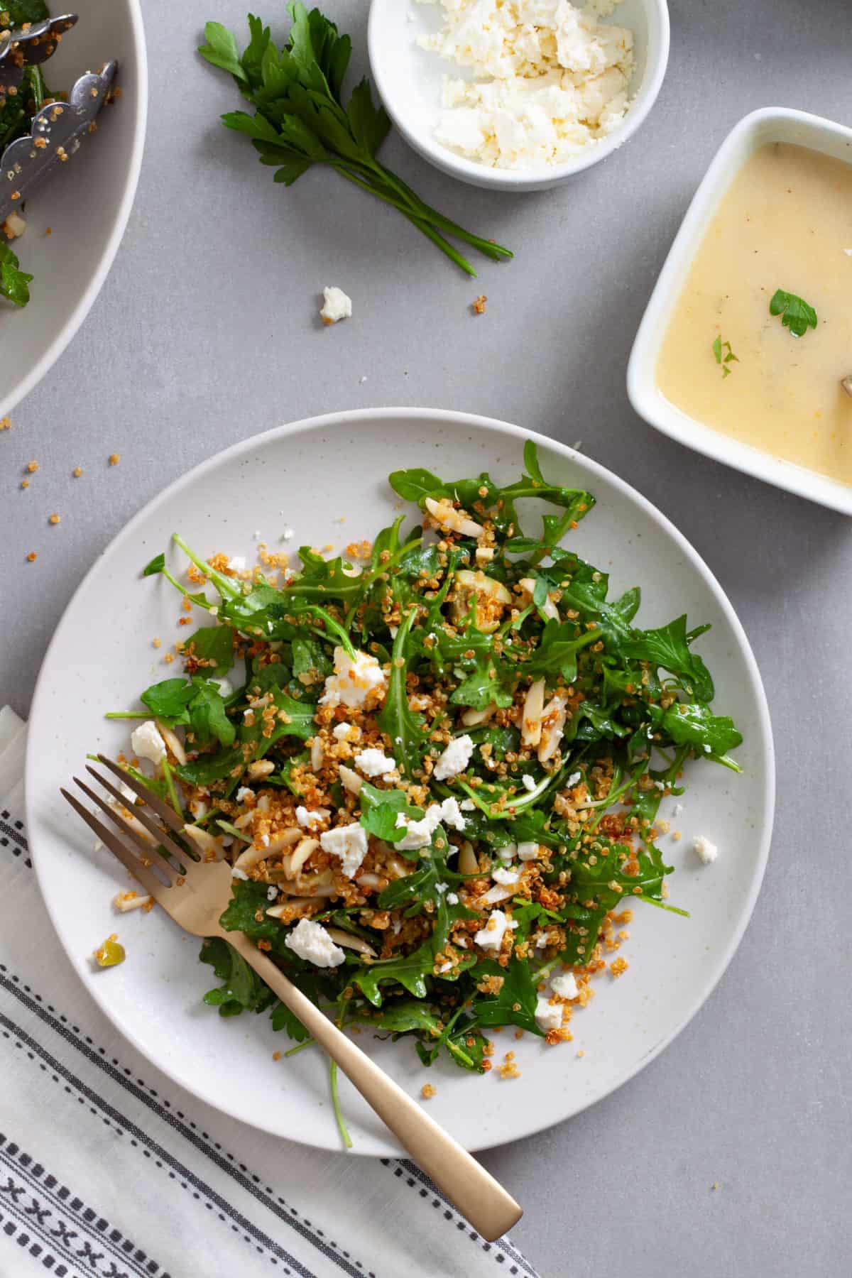 A serving of quinoa and arugula salad on a white plate topped with feta cheese and olives.