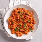 A serving of bulgur pilaf in a white bowl topped with chopped fresh herbs.