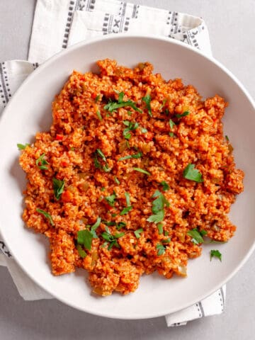 A serving of bulgur pilaf in a white bowl topped with chopped fresh herbs.