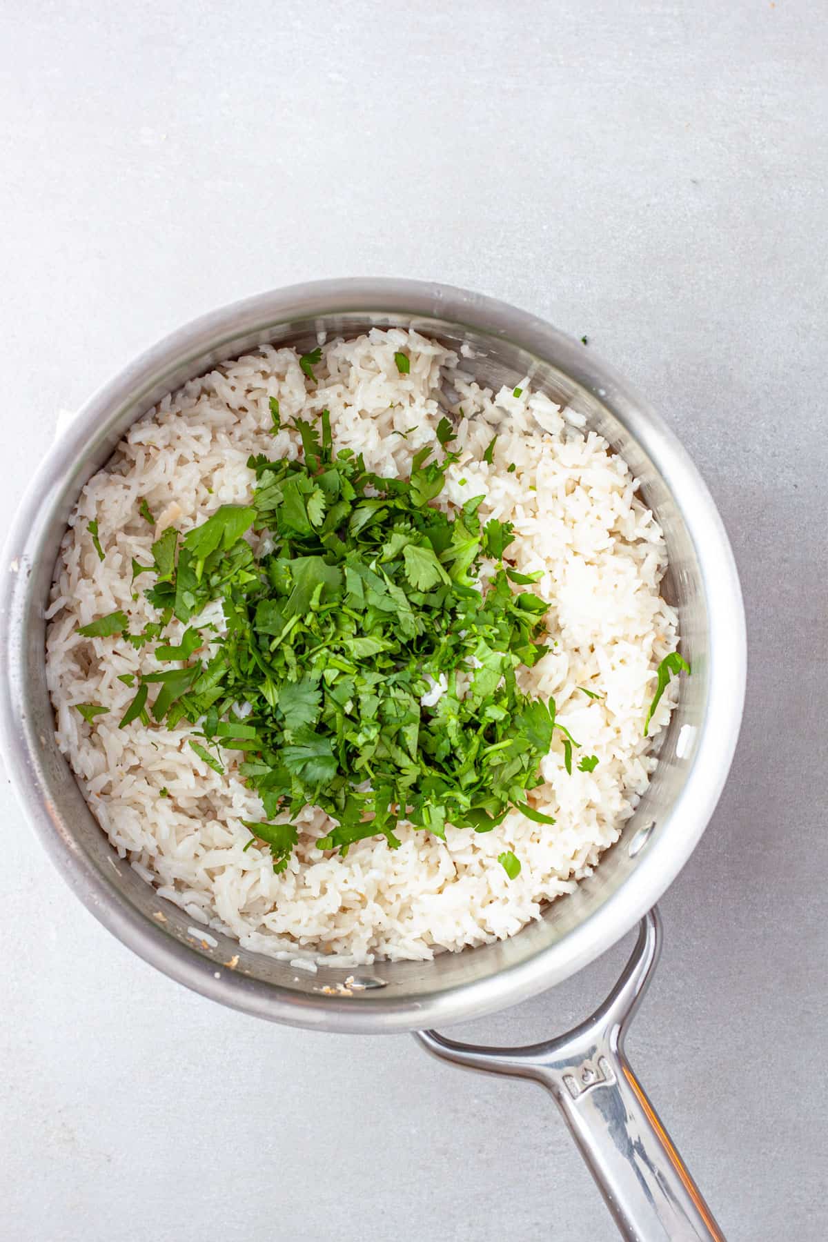 Chopped cilantro added to a saucepan with cooked coconut rice.
