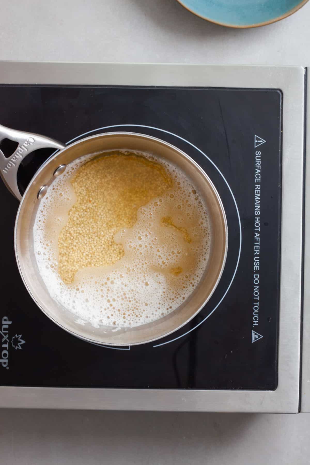 A small pot of water with white quinoa simmering.