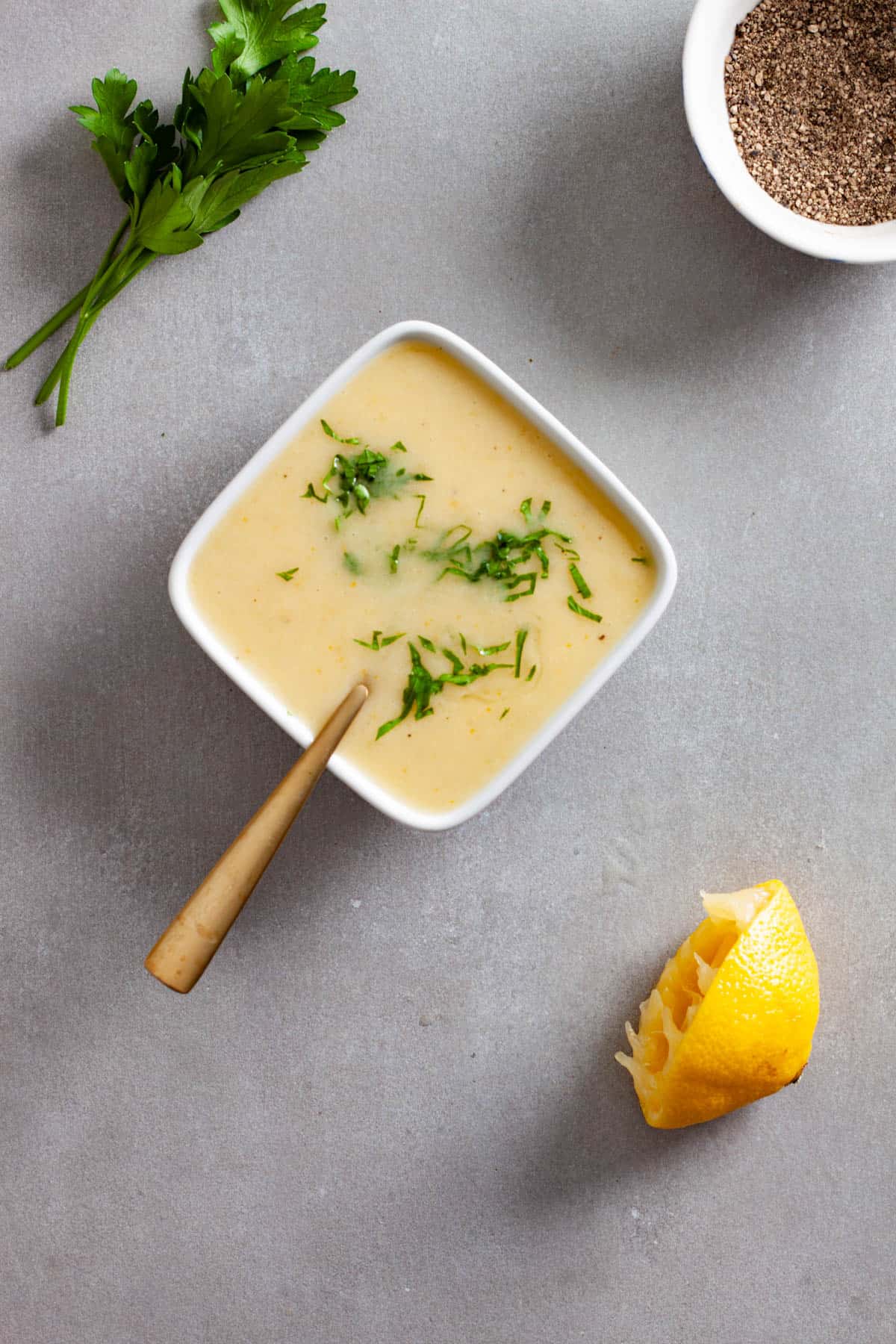 Chopped parsley and black pepper sprinkled on top of a preserved lemon vinaigrette in a small white bowl on a gray table.