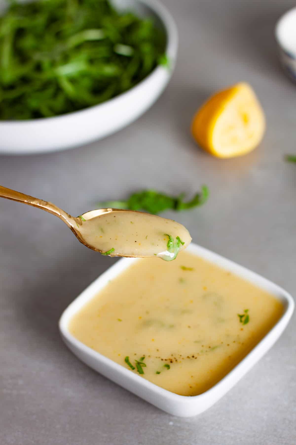 A spoonful of preserved lemon vinaigrette above a bowl of the dressing.