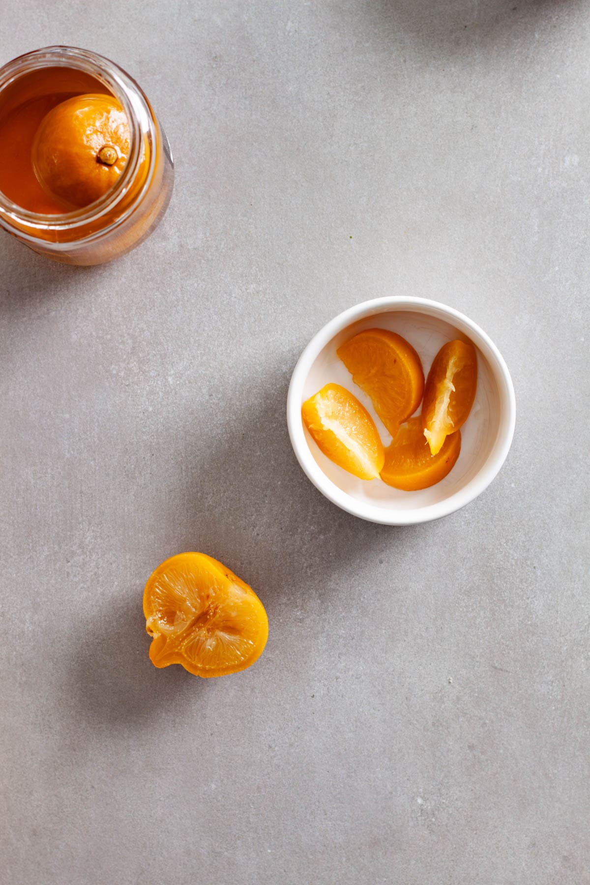 Sliced preserved lemons in a small white bowl with a glass jar of whole preserved lemons to the side.