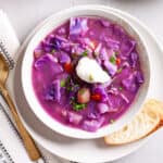 A serving of red cabbage soup in a bowl topped with fresh herbs and sour cream.