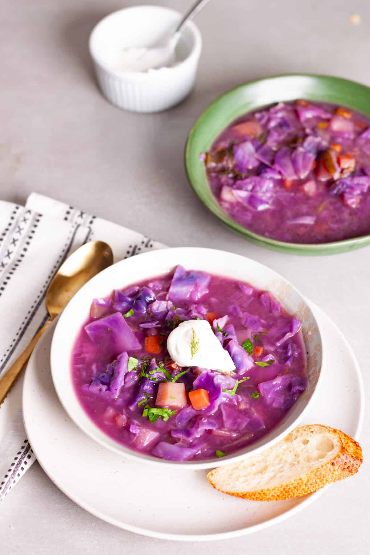 A couple servings of hearty red cabbage soup, one topped with sour cream and fresh herbs.