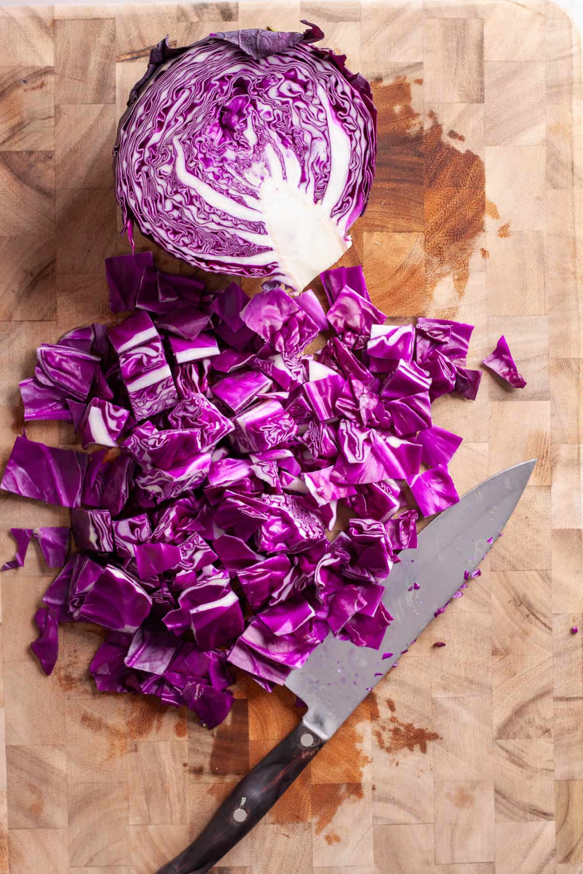 Red cabbage roughly chopped on a butcherblock cutting board.