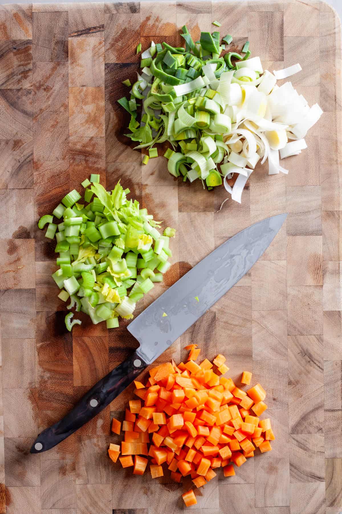 Celery, carrots and a leek chopped on a butcherblock cutting board.