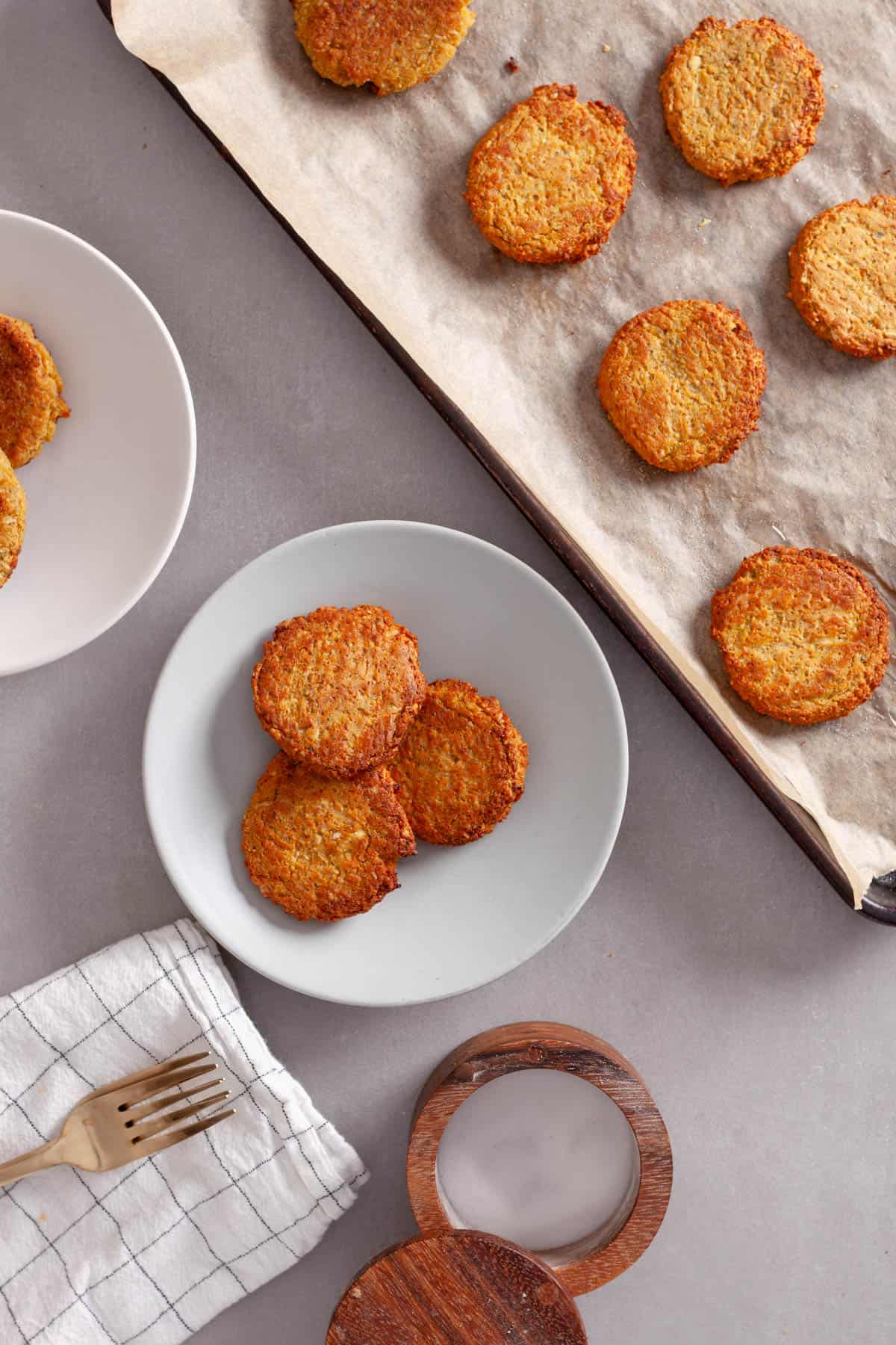 Golden brown cooked red lentil fritters coming off a baking sheet and onto serving plates.