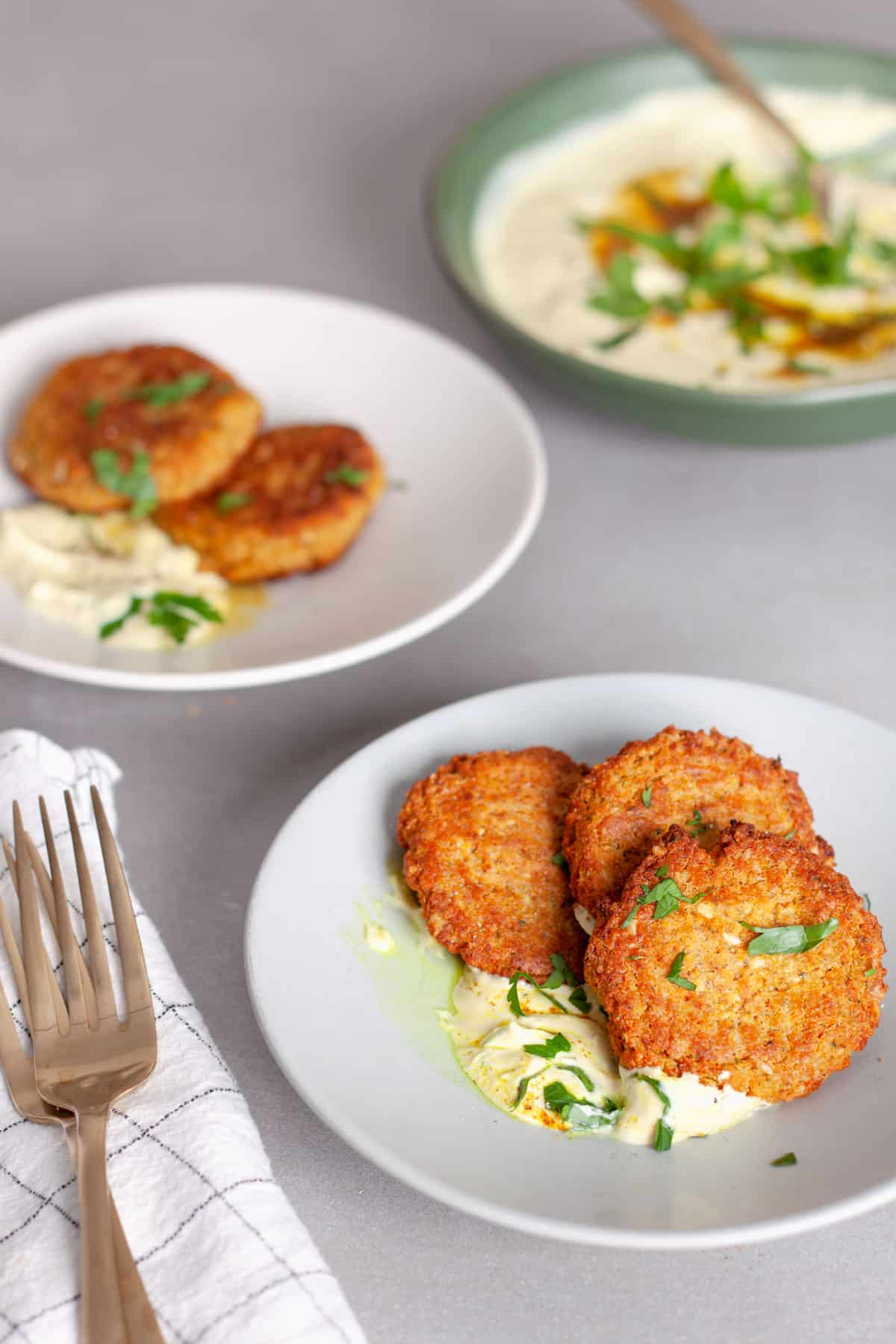 A serving of red lentil fritters with tahini yogurt sauce on a small white plate.