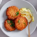 A serving of red lentil fritters on a plate topped with fresh parsley and a tahini yogurt sauce to the side.