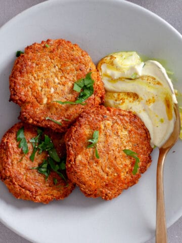 A serving of red lentil fritters on a plate topped with fresh parsley and a tahini yogurt sauce to the side.