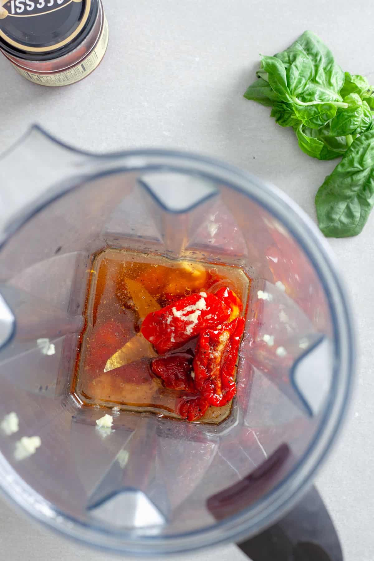 An overhead shot of a blender with sun-dried tomatoes, oil, red wine vinegar, garlic, salt and pepper inside.