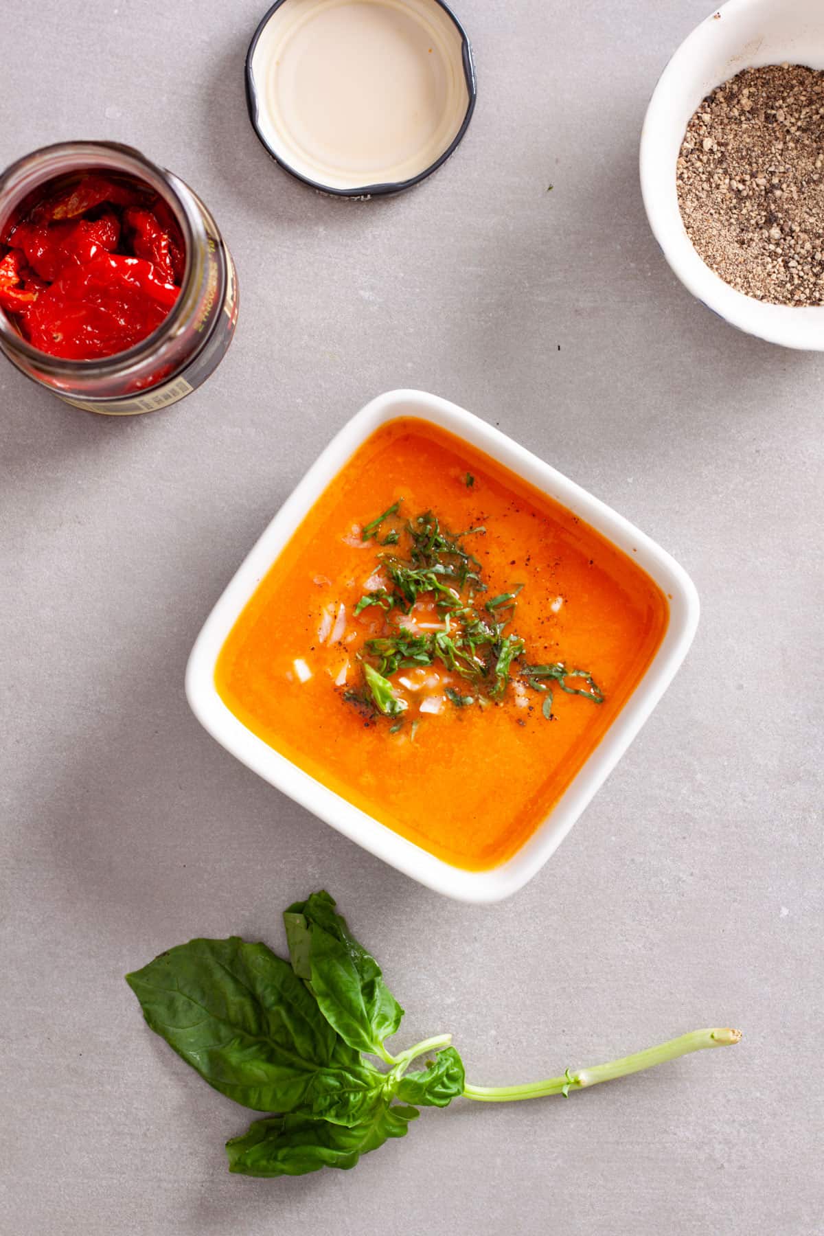 A small white bowl with sun-dried tomato dressing topped with chopped basil leaves and minced shallots.