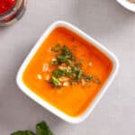 A small white bowl with sun-dried tomato dressing topped with chopped basil leaves and minced shallots.