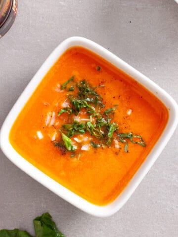 A small white bowl with sun-dried tomato dressing topped with chopped basil leaves and minced shallots.