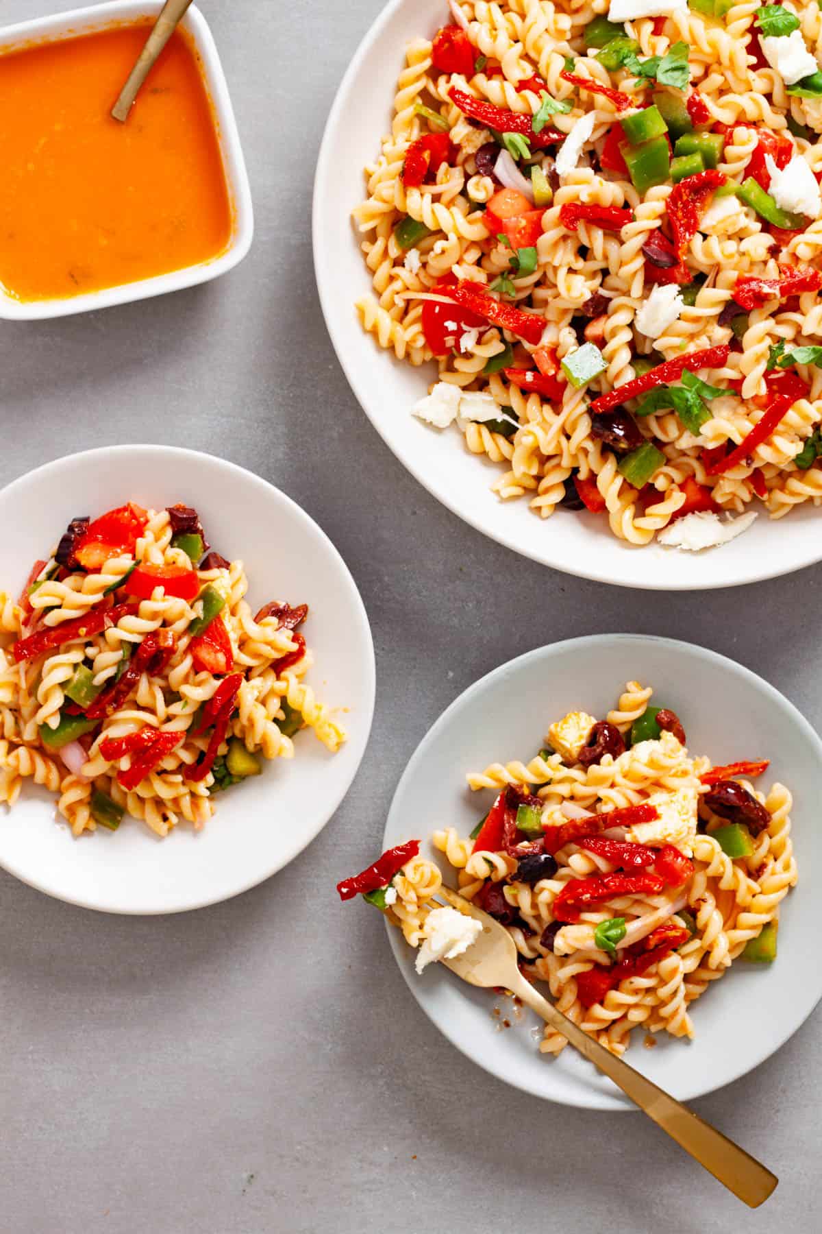 A couple small plates with sun-dried tomato pasta salad and a large mixing bowl with more salad to the side.