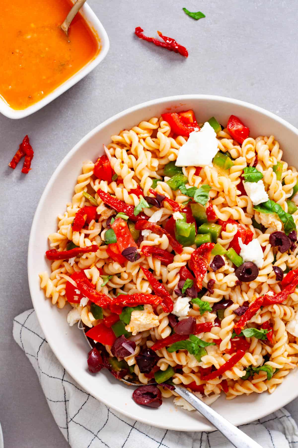 A large white bowl with homemade sun-dried tomato pasta salad on a gray table.