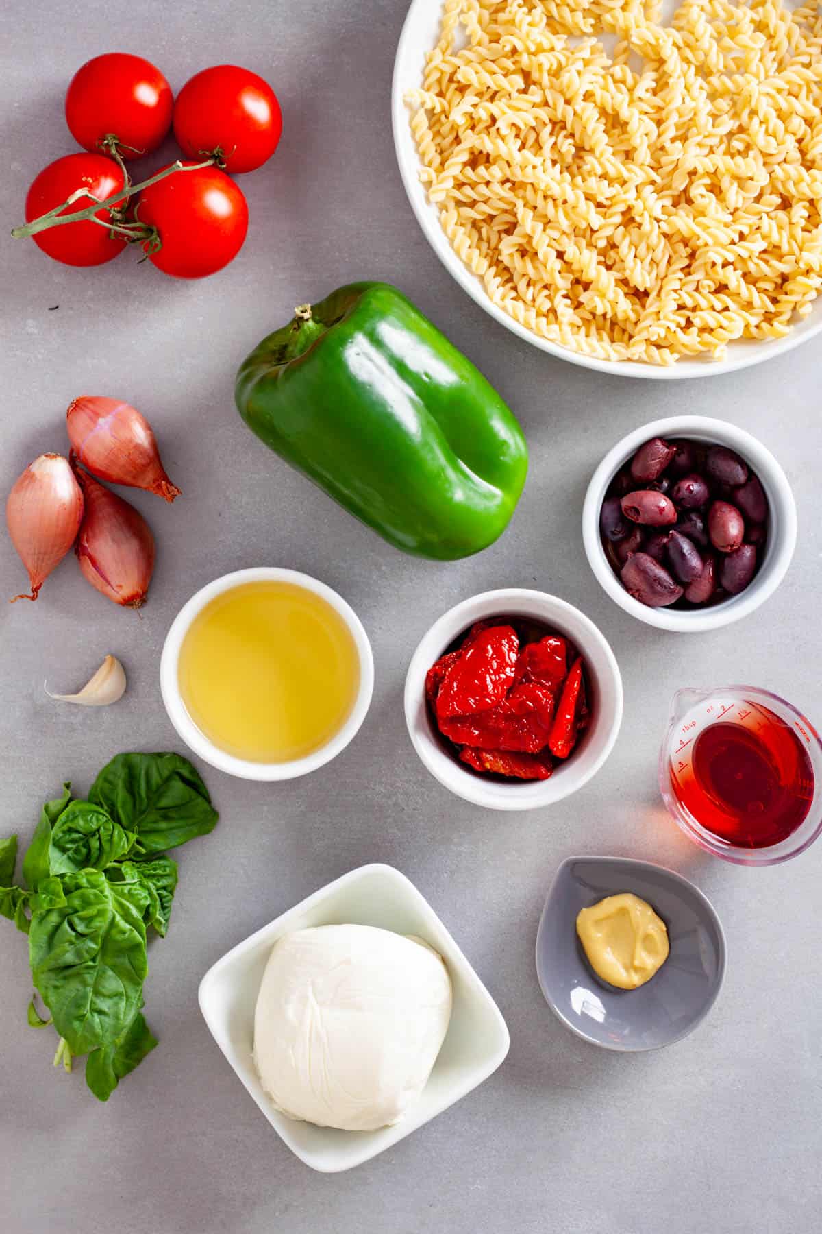 Ingredients for a sun-dried tomato pasta salad on a gray table.