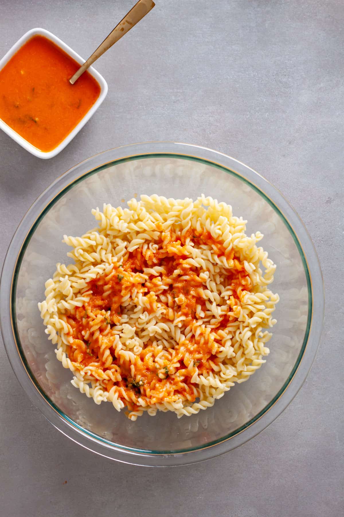 Pasta in a large mixing bowl topped with homemade sun-dried tomato vinaigrette.