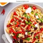 A large white bowl with homemade sun-dried tomato pasta salad on a gray table.