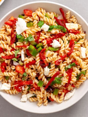 A large white bowl with homemade sun-dried tomato pasta salad on a gray table.