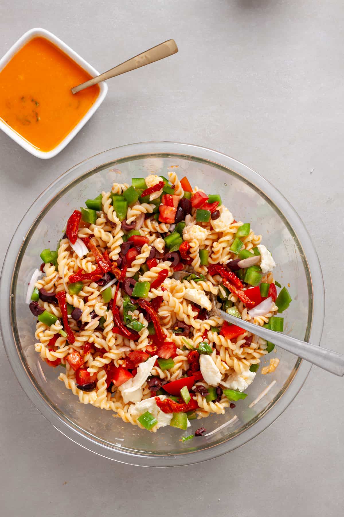 Sun-dried tomato pasta salad in a large mixing bowl with vegetables, cheese and basil.
