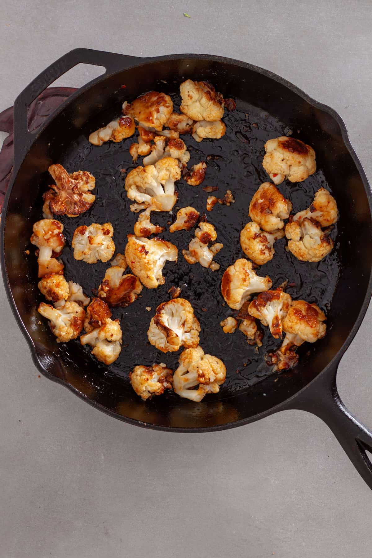 Seared cauliflower florets tossed with sweet chili sauce in a cast iron skillet.