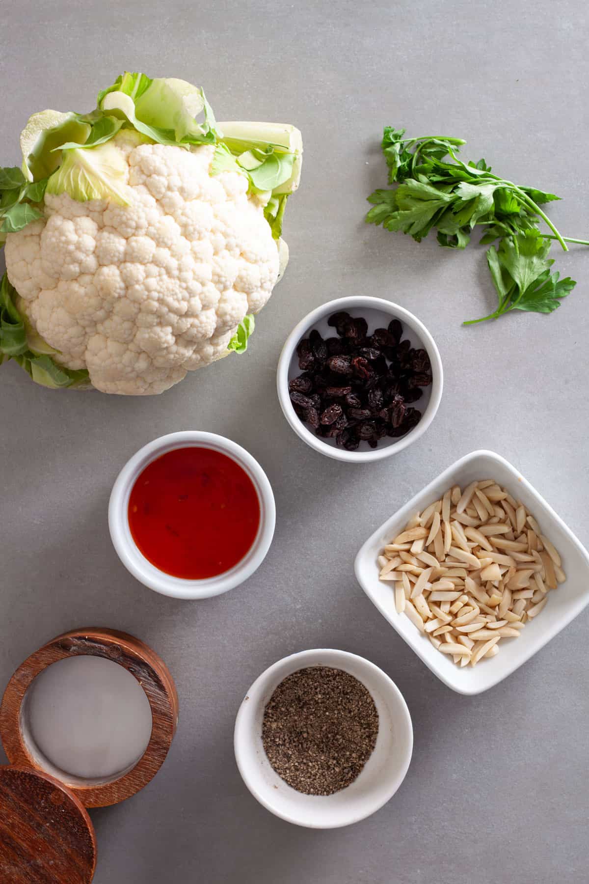 Ingredients for sweet chili roasted cauliflower with almonds on a gray table.