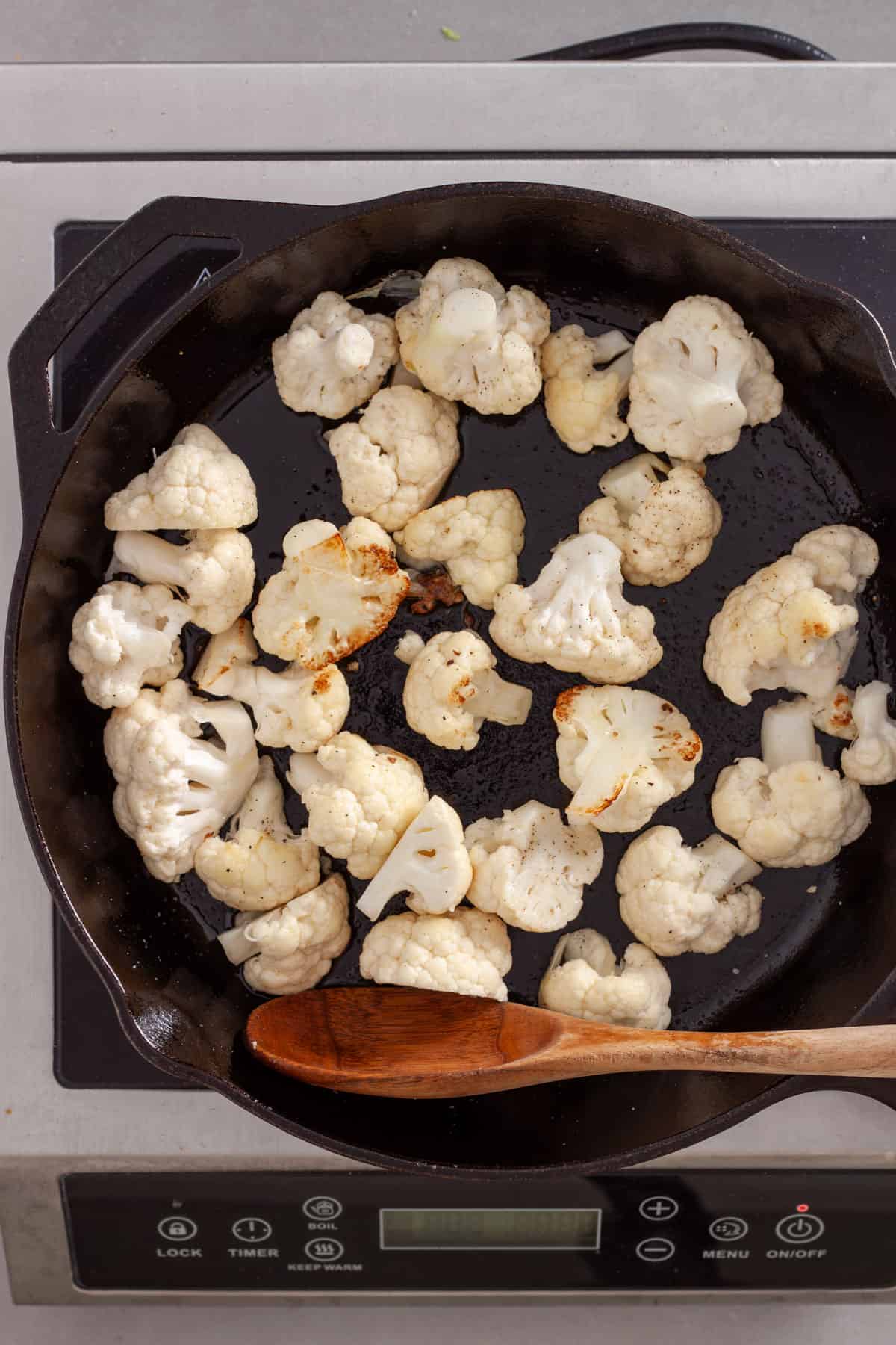 Cauliflower florets getting seared in a large cast iron skillet.